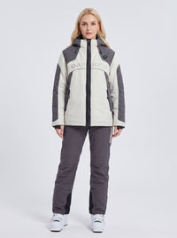 A woman modeling a heated ski jacket and matching ski pants set. The jacket is off-white and dark gray with a black zipper and 'ANNIOU' printed across the chest.