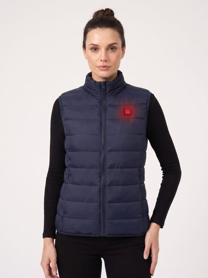 A woman modeling a navy blue insulated puffer vest over a black long-sleeve top, shown against a plain light gray studio background. A small red square logo is visible on the left chest of the vest.