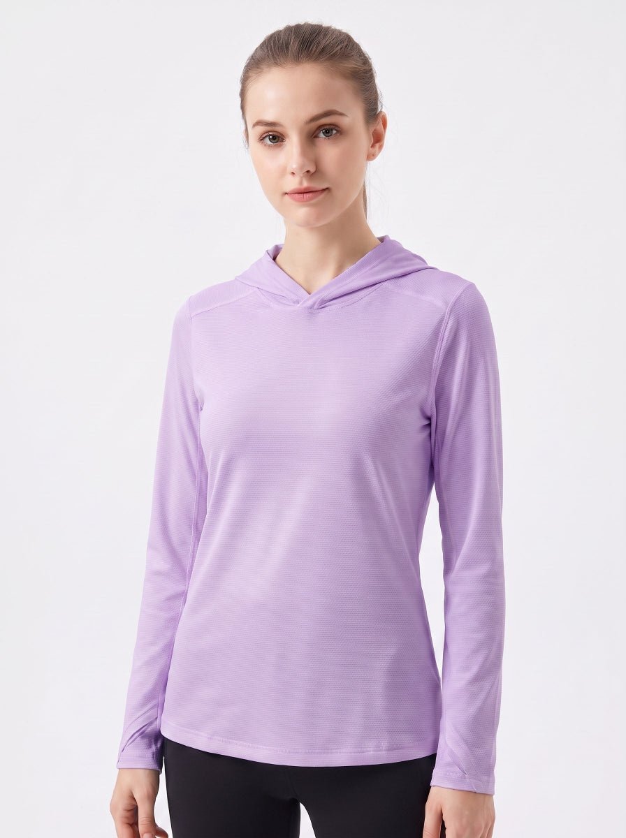 A woman wearing a light purple long-sleeve athletic hooded top, paired with black leggings, standing against a plain light gray studio background.