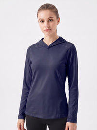 A woman wearing a navy blue long-sleeve hooded athletic top, standing against a plain light gray studio background.